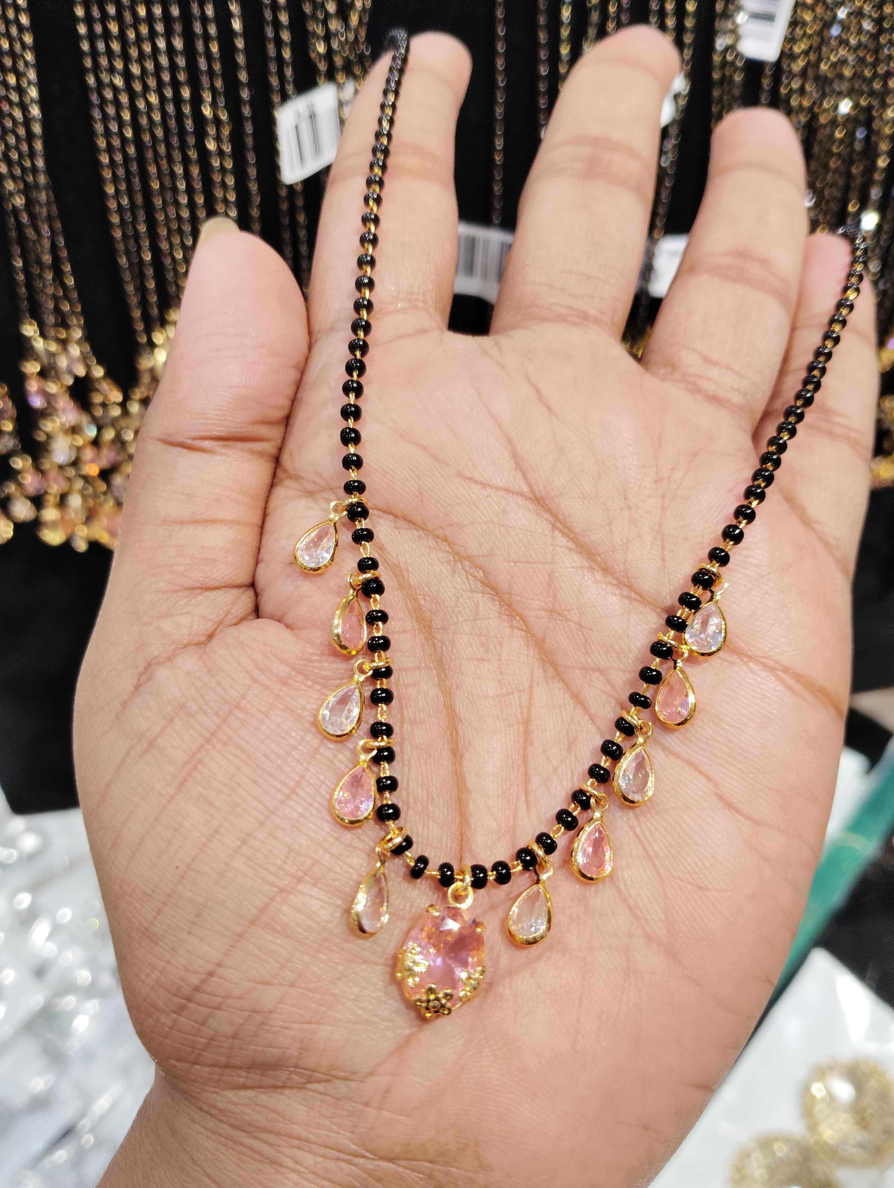 mangalsutra with black beads and pink teardrop dangling pendants held on a hand