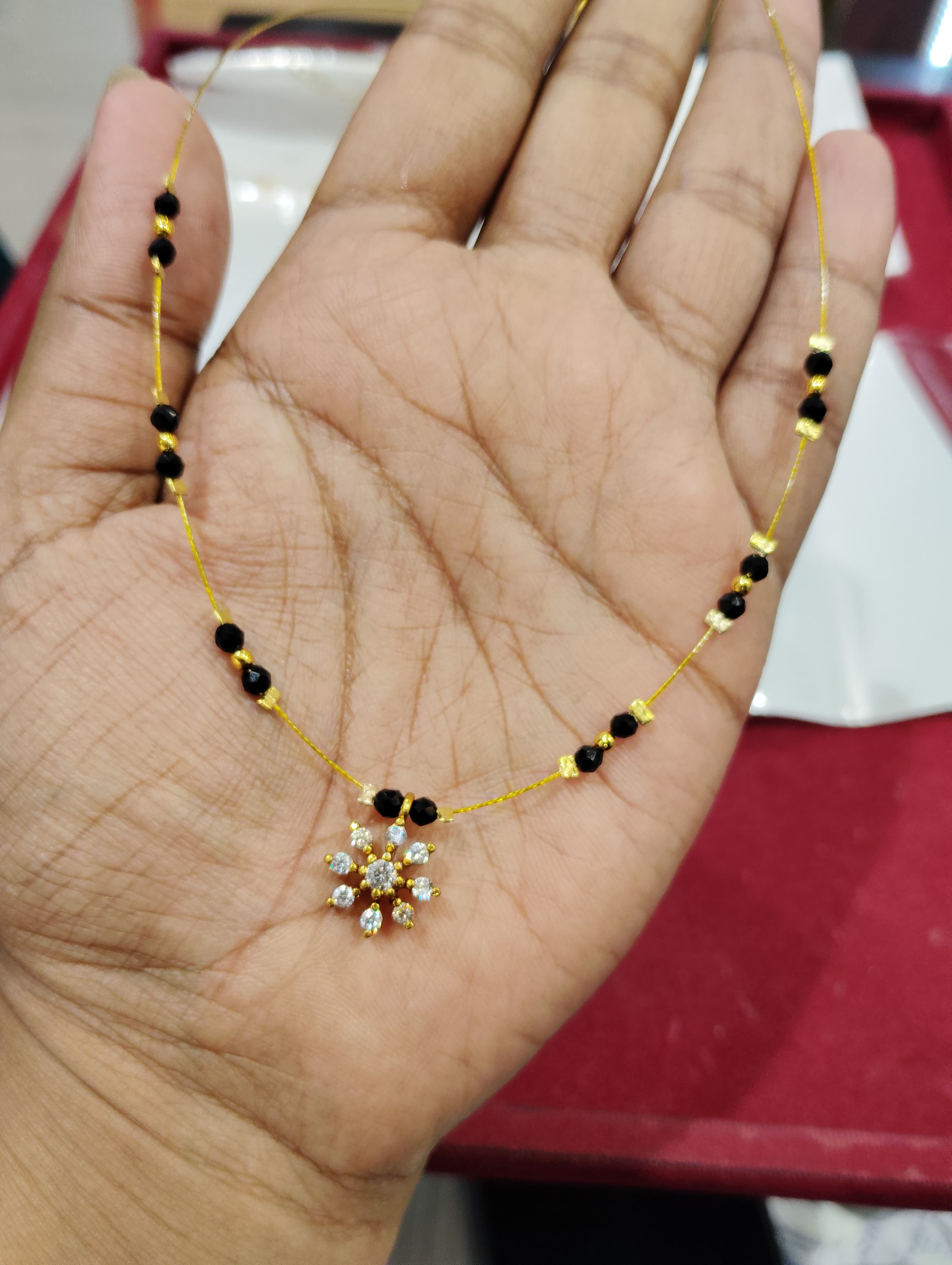 Fine mangalsutra with small black beads and a flower-shaped clear-stone pendant on a gold-coloured thread