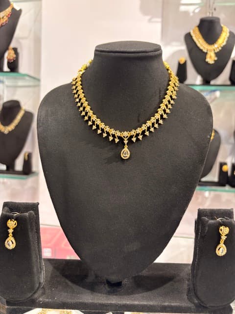 Gold-coloured leaf-link necklace with teardrop pendant on black display and matching drop earrings