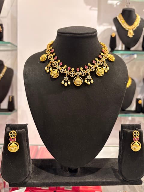 Gold-tone short necklace with coin pendants and matching drop earrings on black display