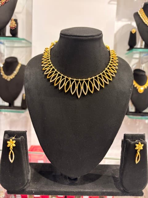 Gold-tone marquise-shaped linked choker necklace with matching floral drop earrings on black display bust