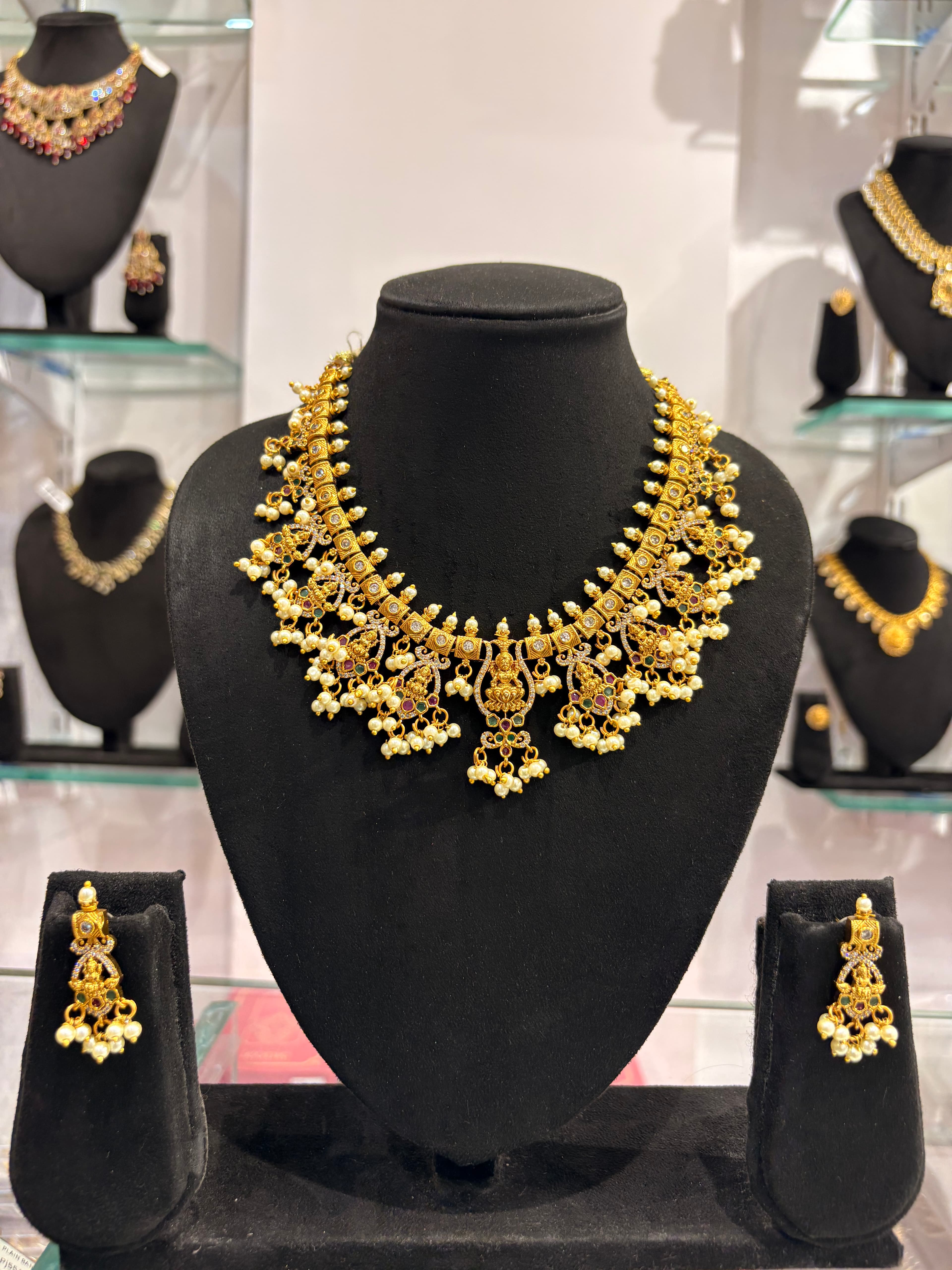 Gold-tone temple-style necklace with multiple white pearl drop clusters on black bust