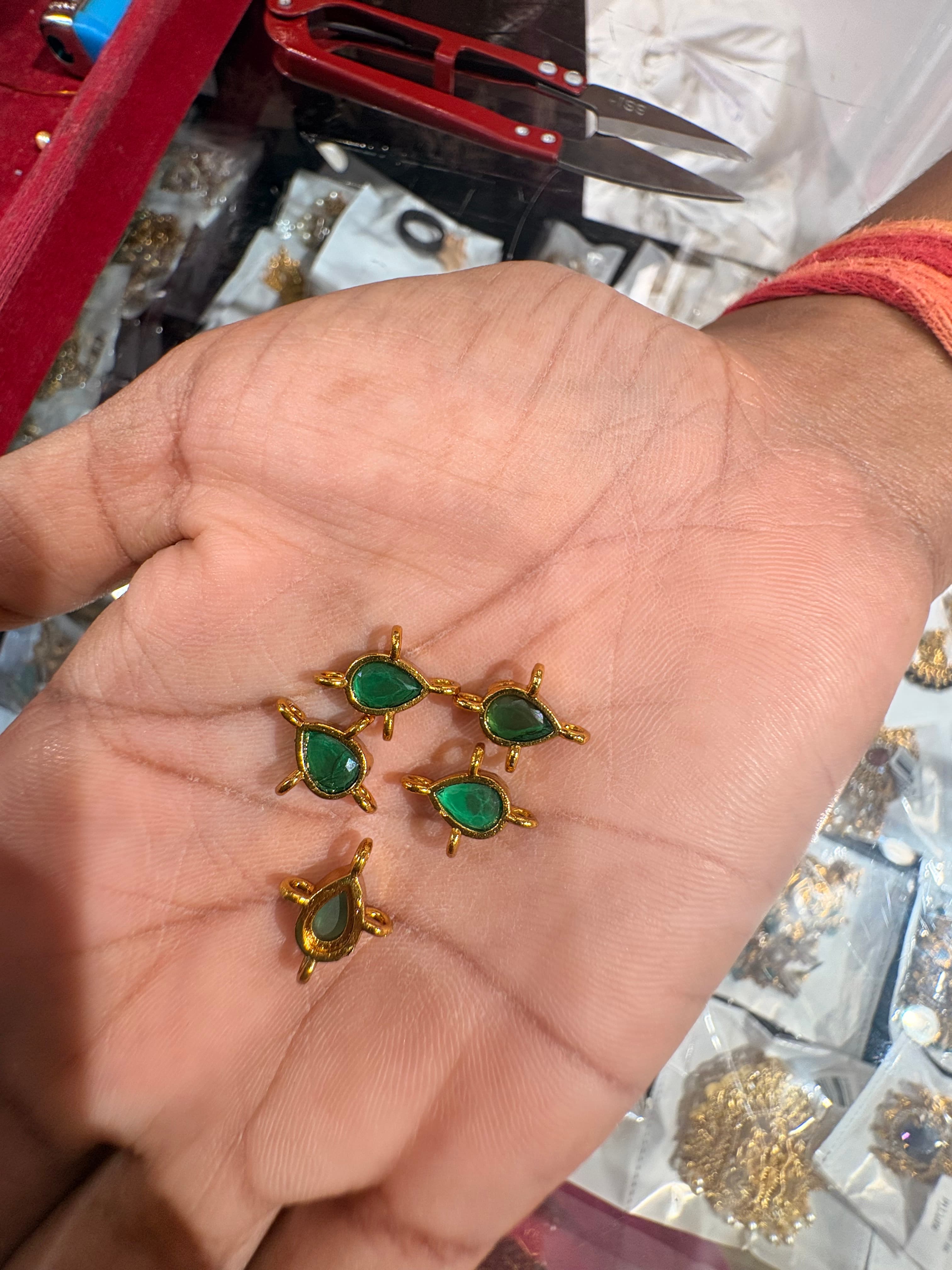 Small green teardrop connector bits with gold-tone frames and three loop points held in a hand