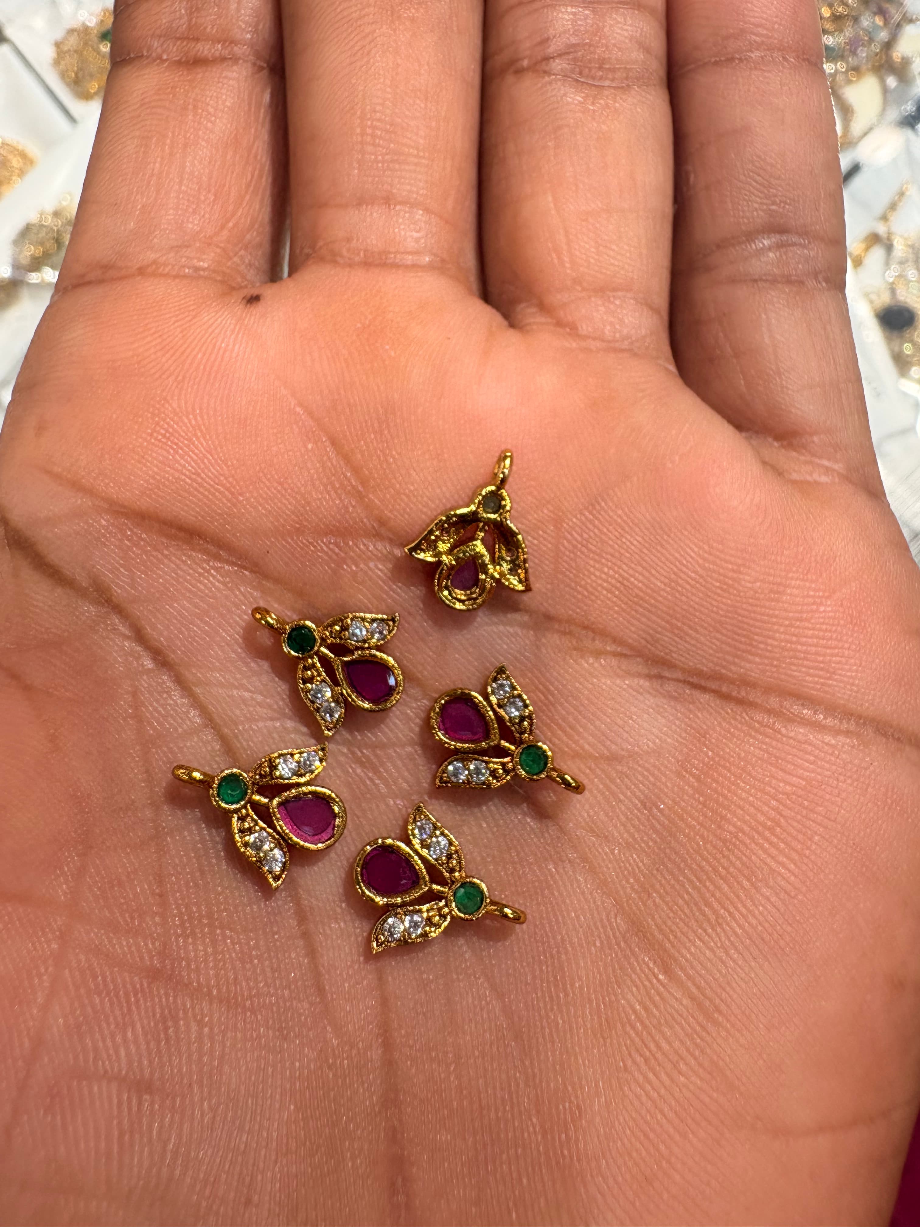 Tiny gold-coloured floral bits with pink teardrop, green round accent and clear sparkle details on a palm