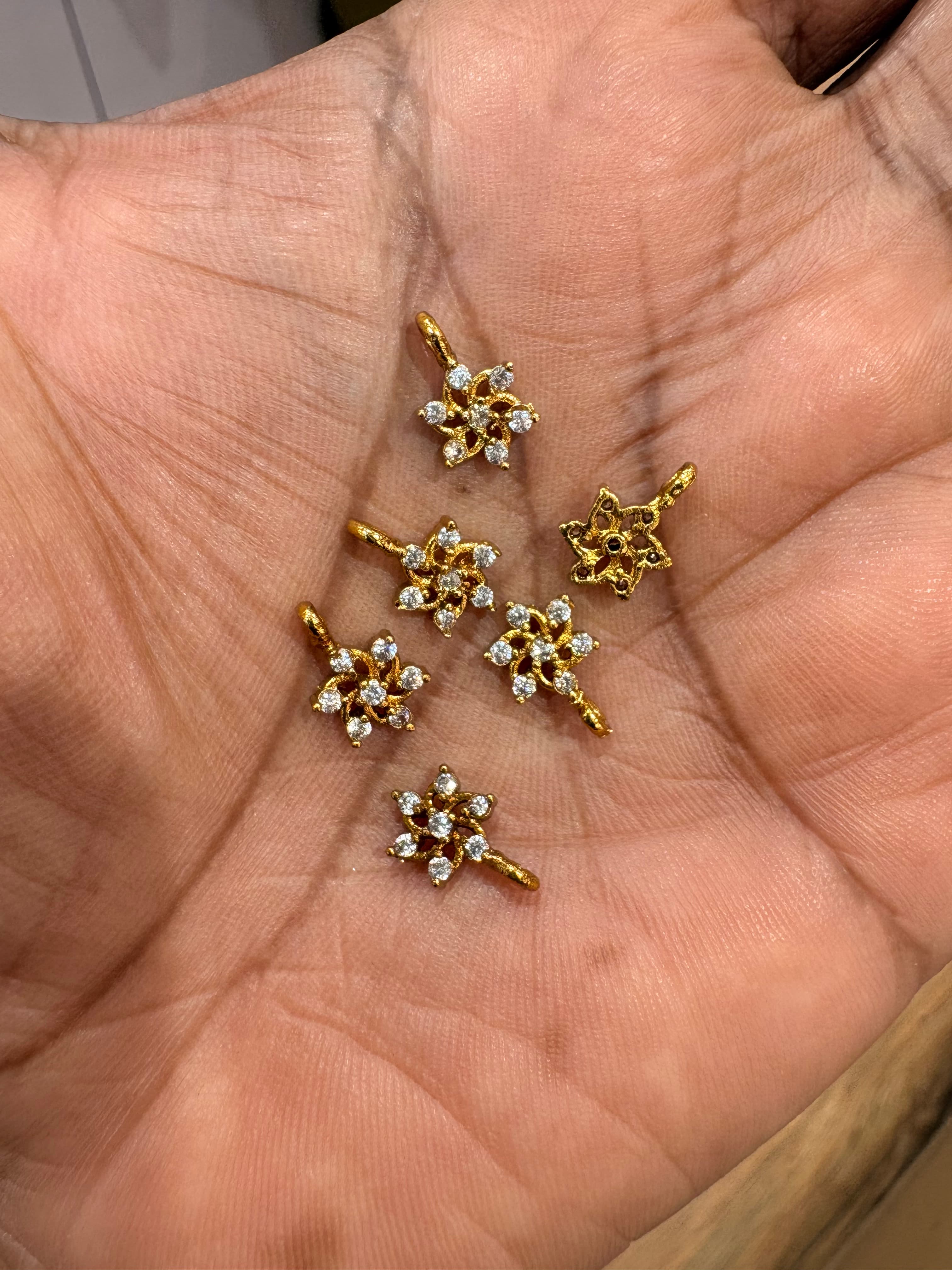 Small gold-tone floral pendant bits with clear round decorative accents on a palm