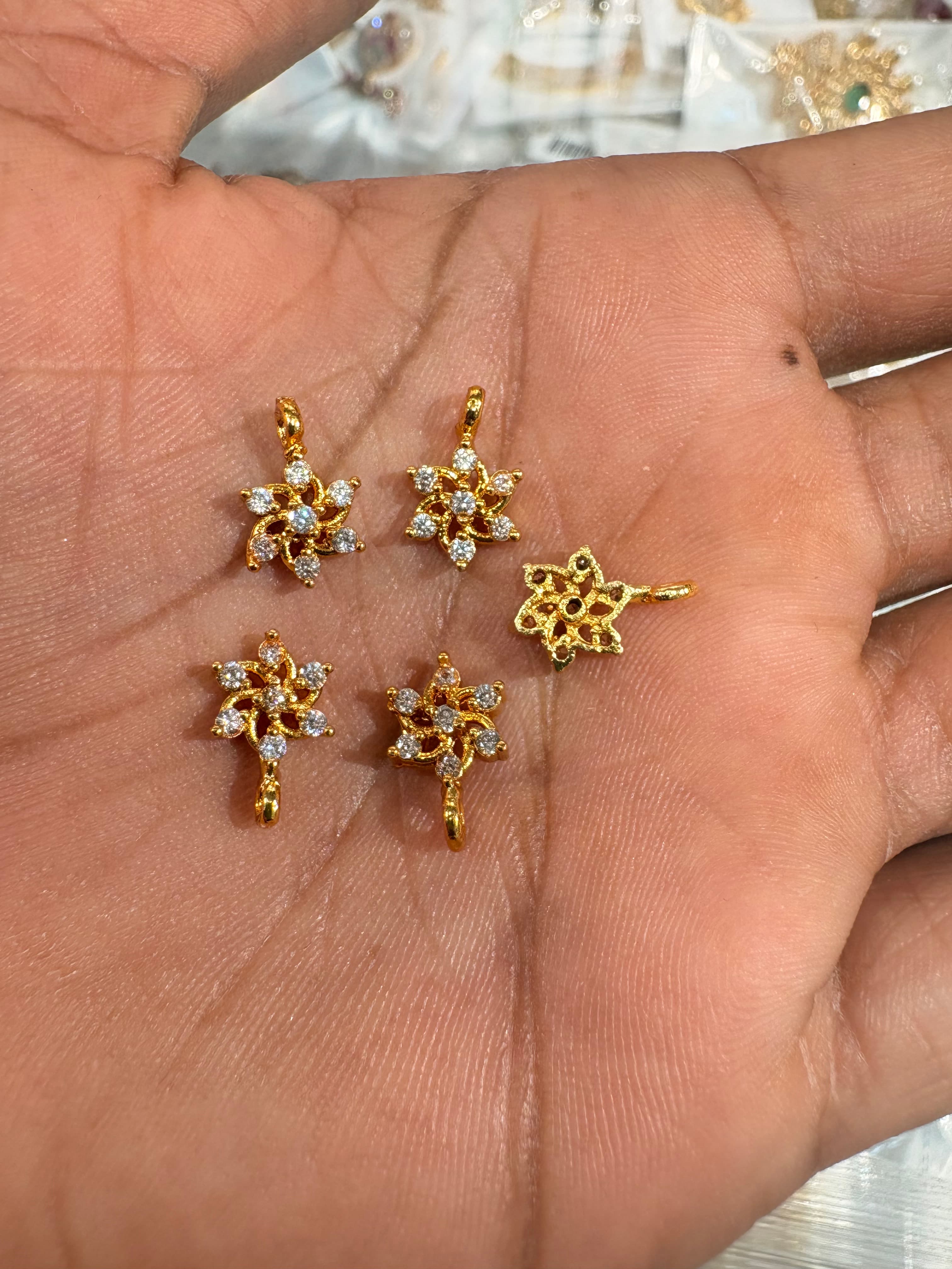 Small gold-tone six-petal floral pendant bits with clear round accents and top loops on a hand