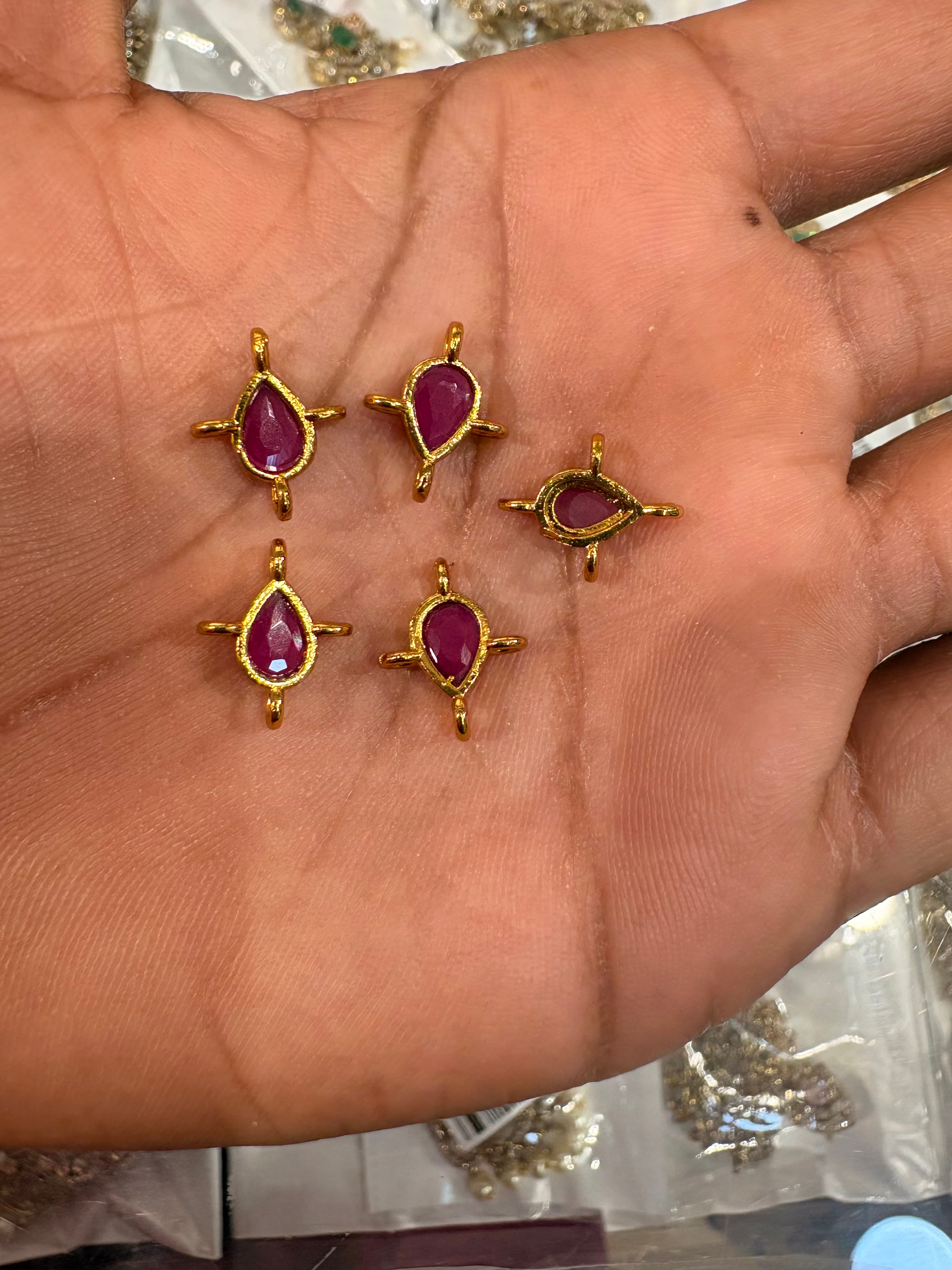 Small teardrop pink-red connector bits in gold-colour metal frames with attachment loops