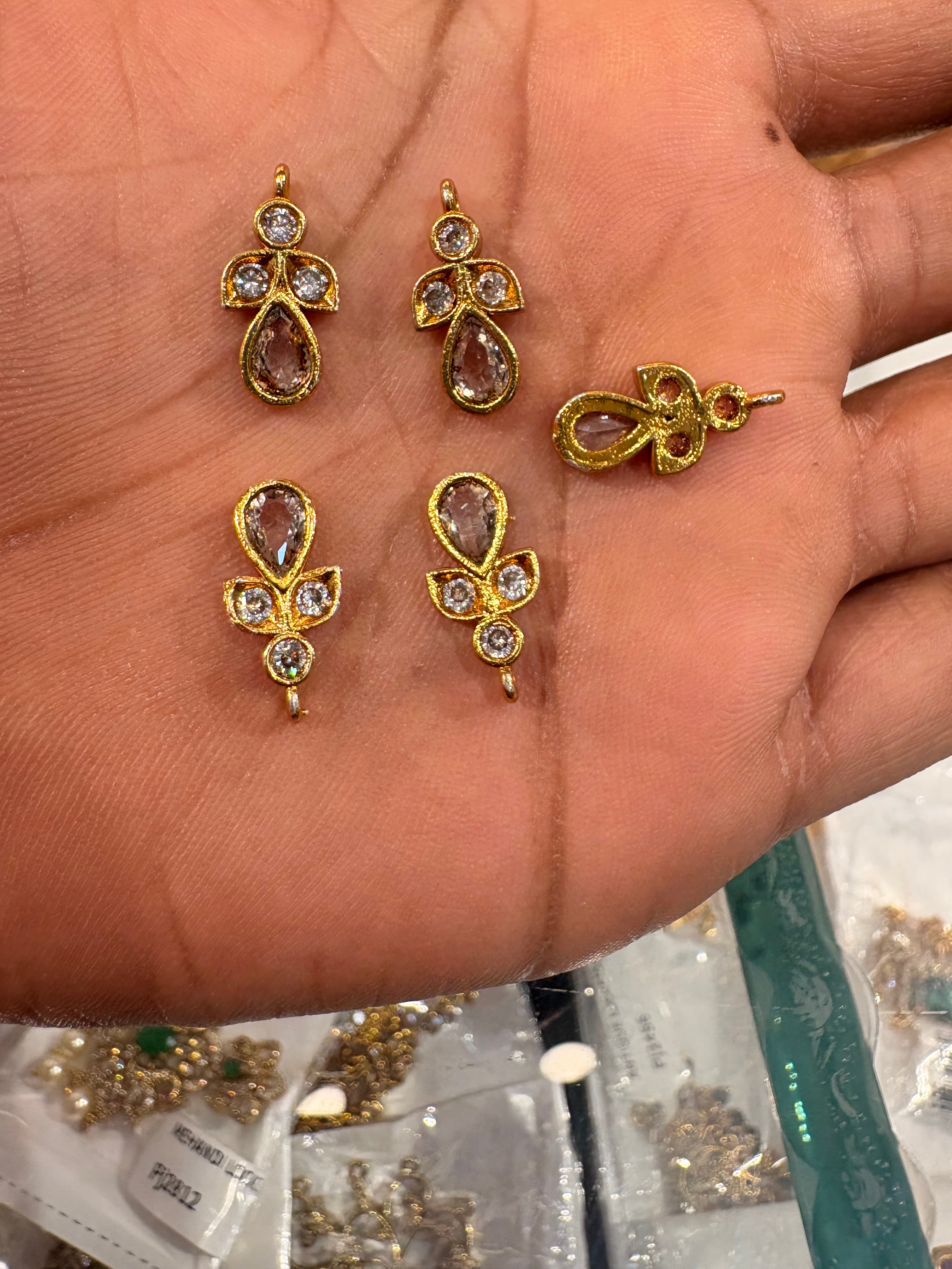 Gold-tone teardrop jewellery connectors with clear round accents on a hand