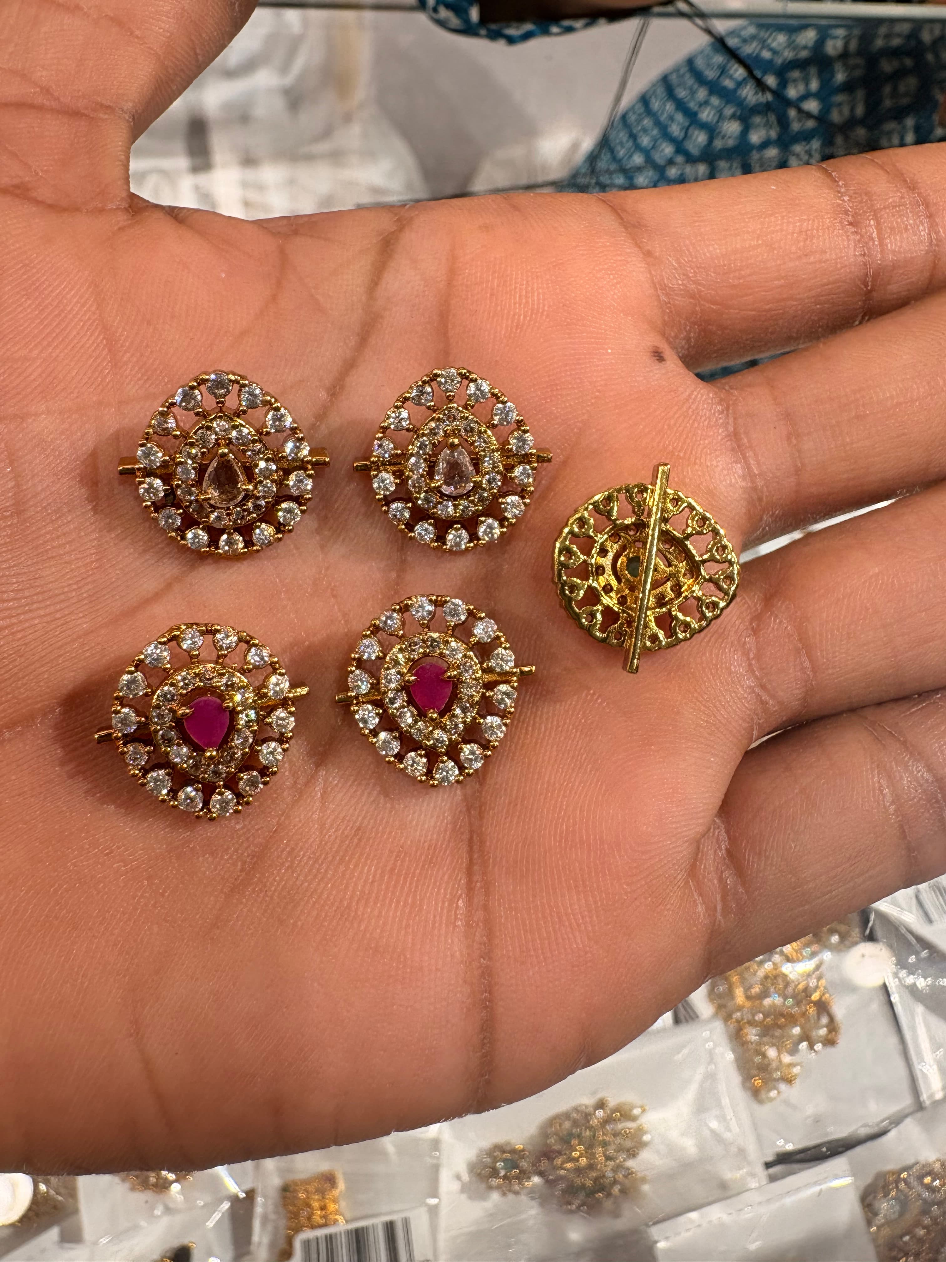 Round gold‑tone decorative bits with clear crystals and teardrop coloured centres on a hand