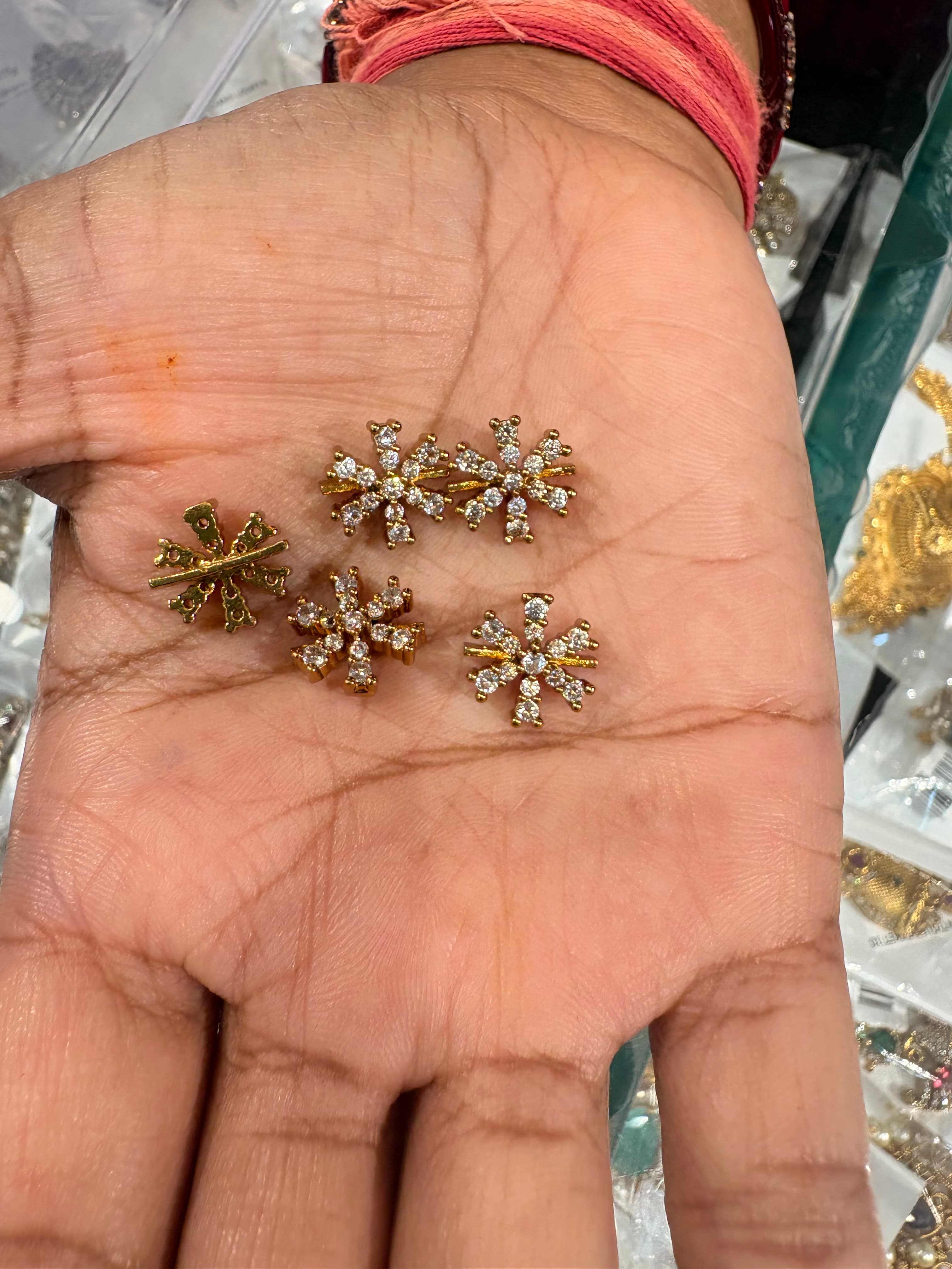 Small gold-tone snowflake decorative bits with clear round accents on a palm