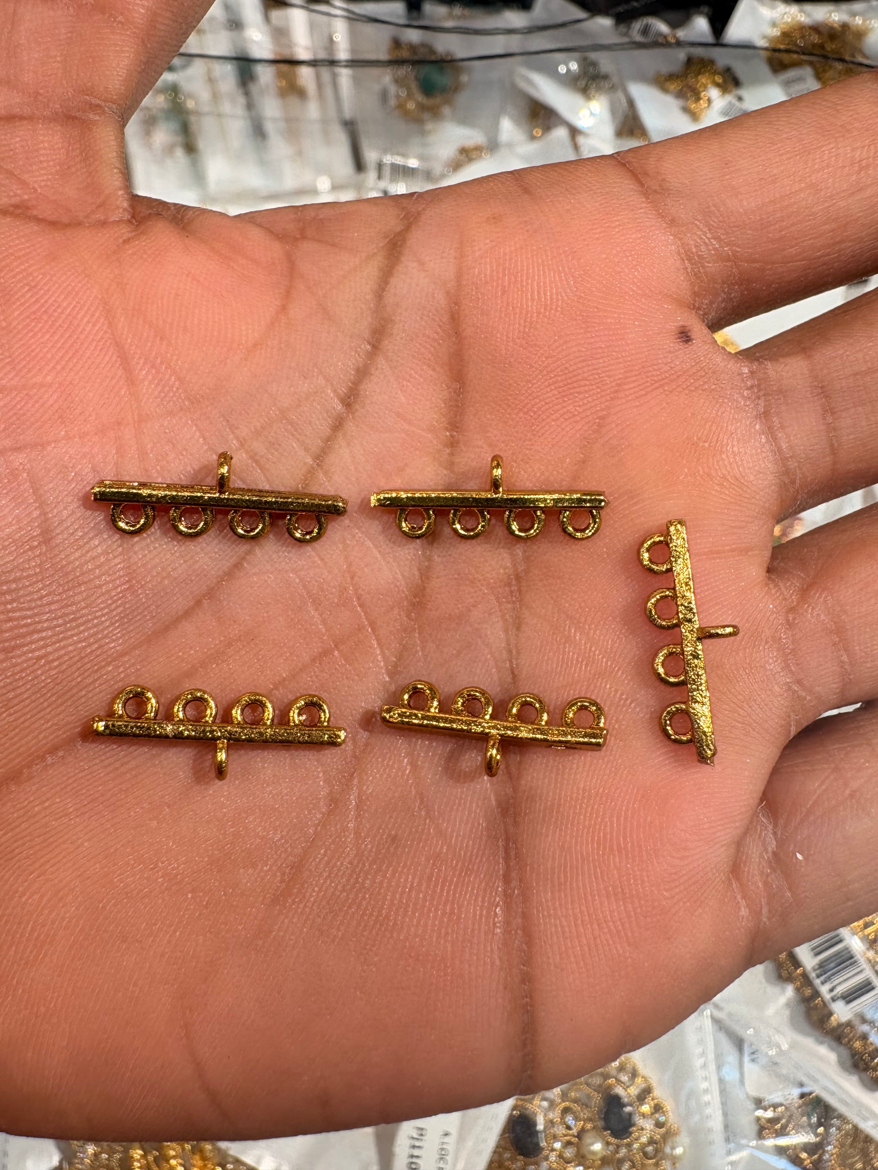 Small gold-coloured horizontal jewellery connectors with four round loops shown on a palm