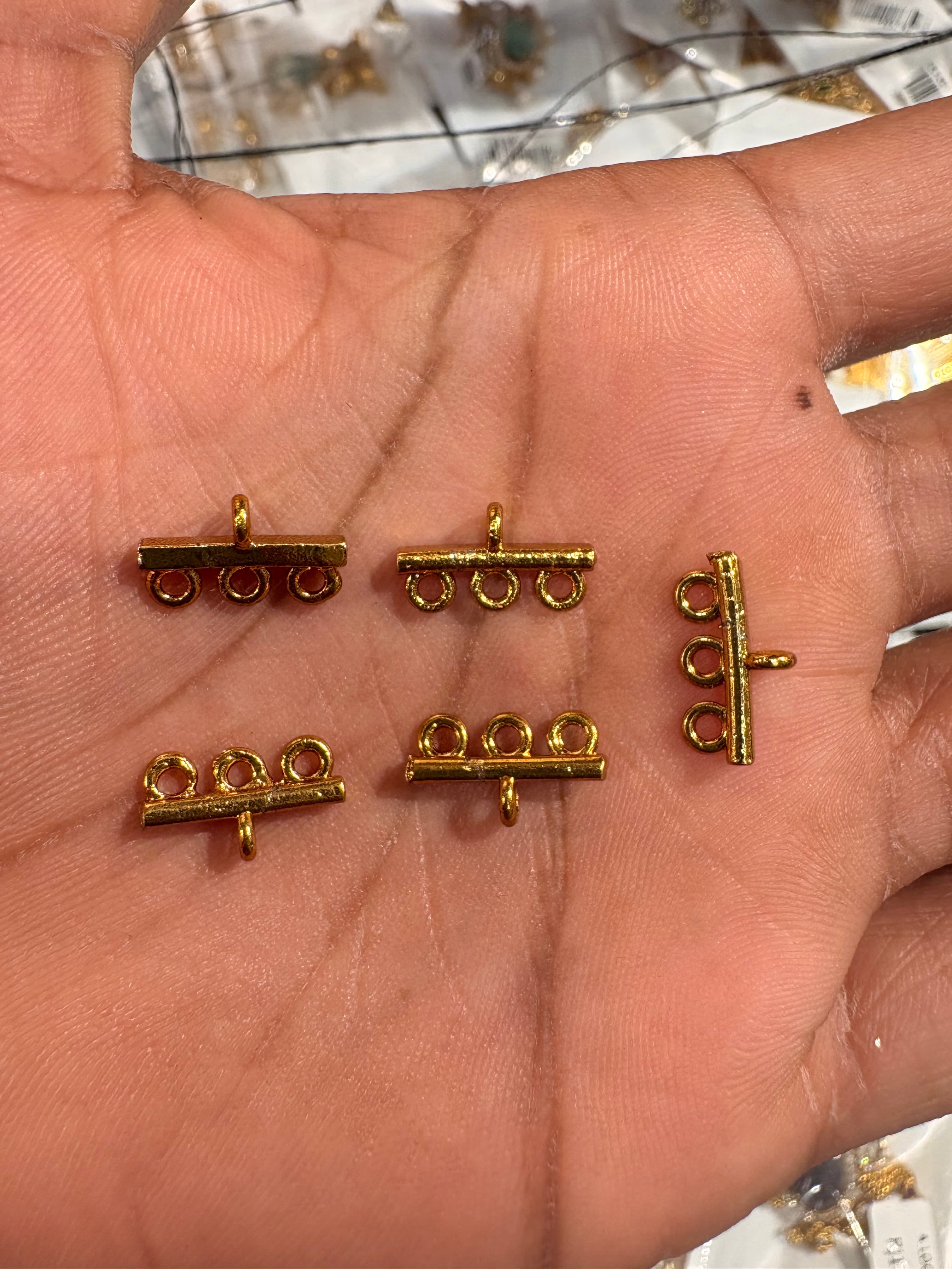 Small gold-colour three-loop jewellery connectors on a palm for scale