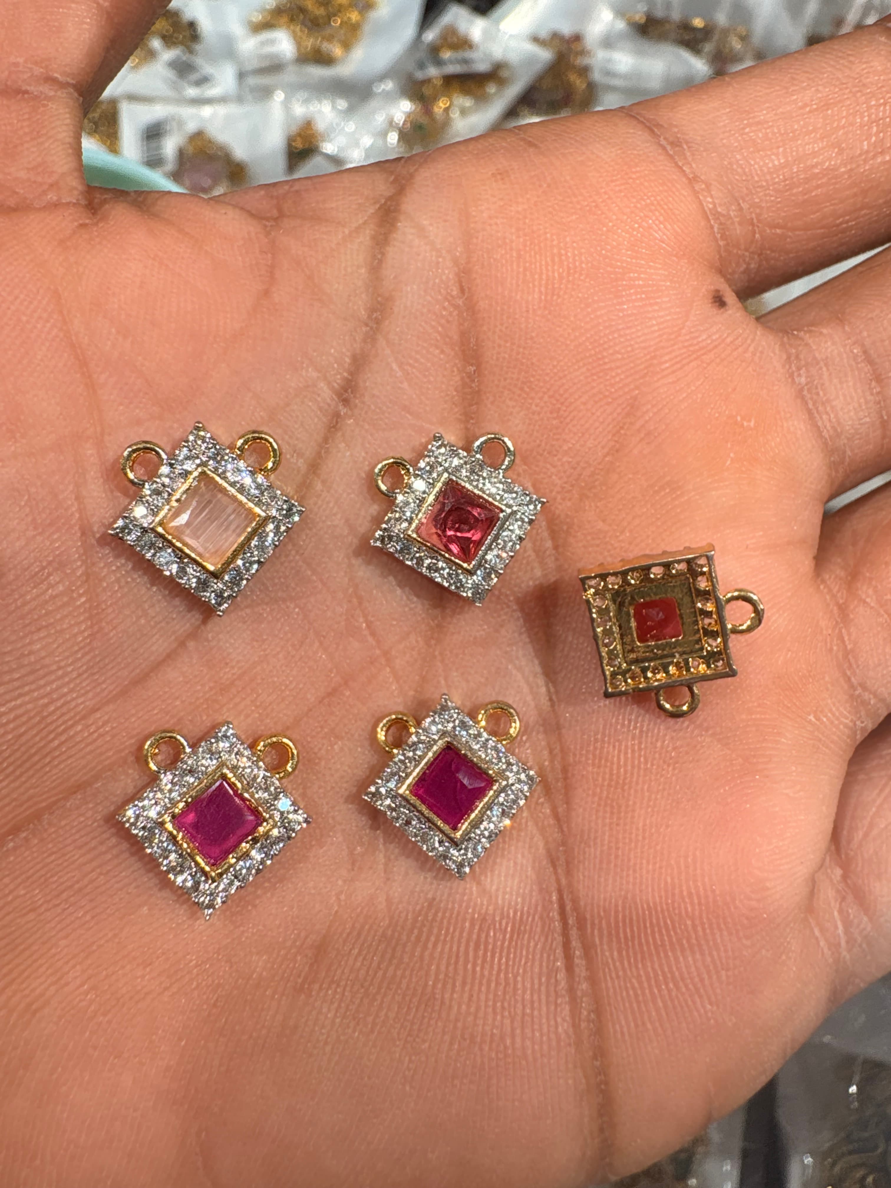 small square connector charms with pink centre and surrounding clear accents held on a palm