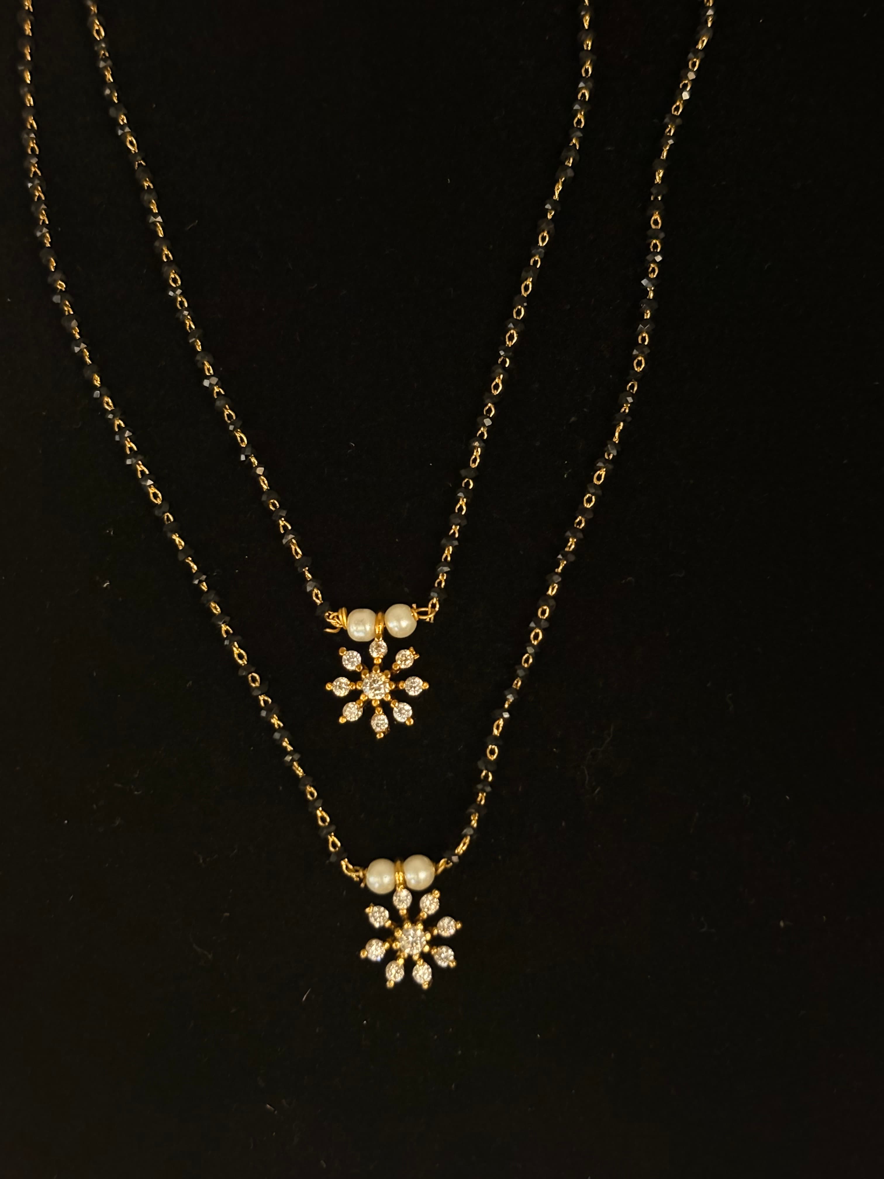 Layered mangalsutra with black beads, gold-toned links and small floral pendants with white bead accents