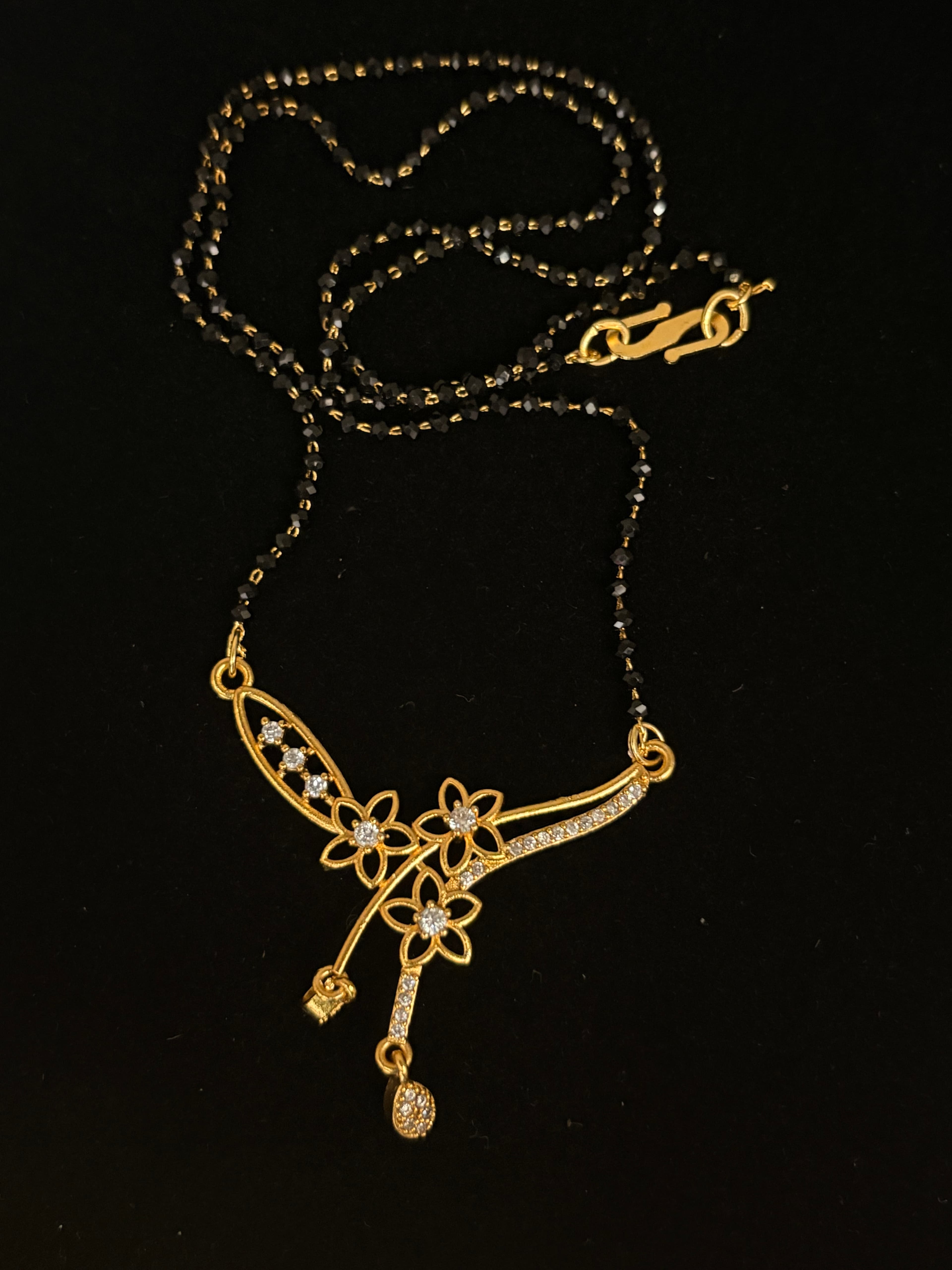 Mangalsutra with twin black bead strands and a gold-tone floral pendant with clear accents