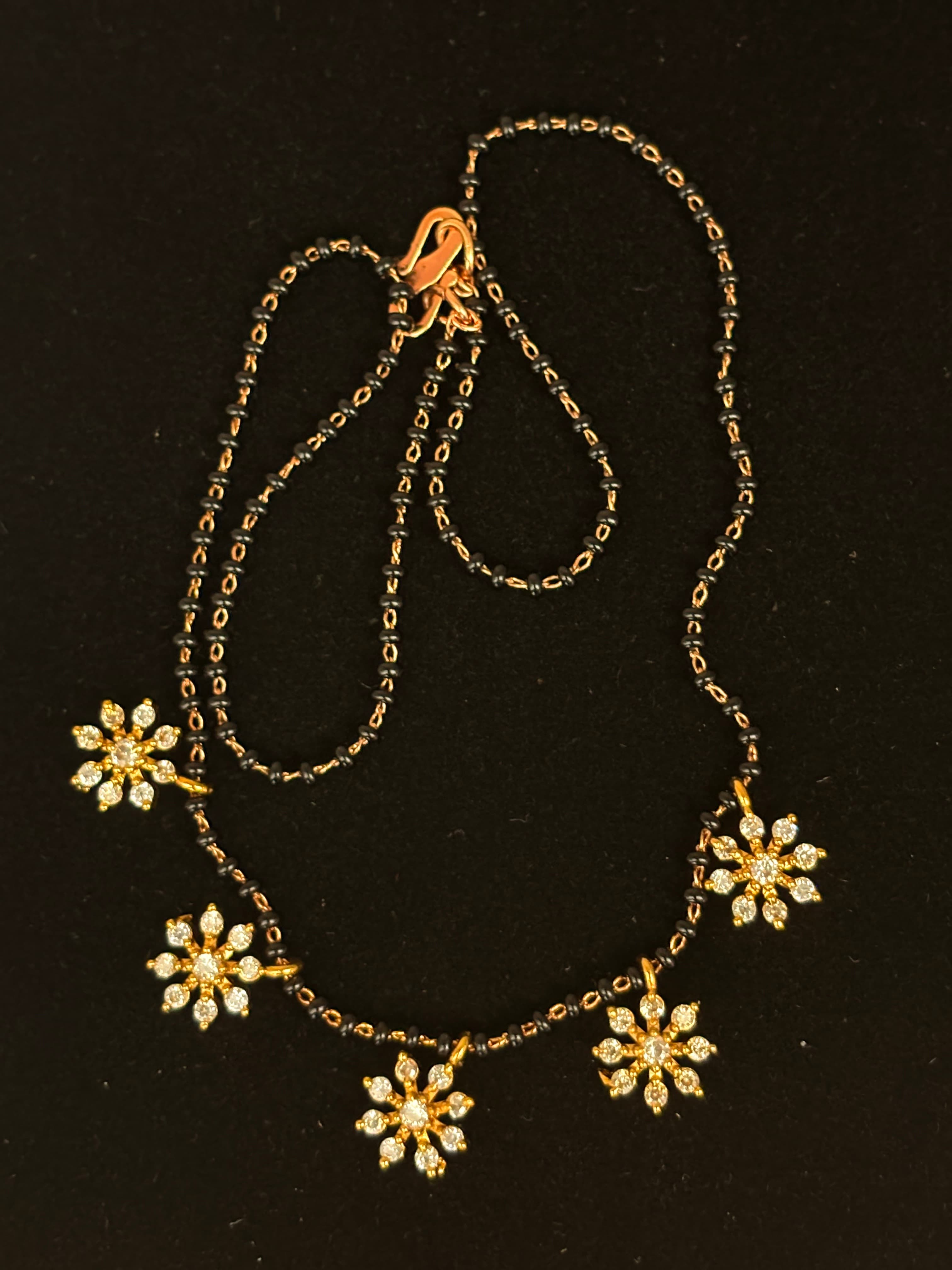 Black bead mangalsutra chain with gold-coloured links and flower-shaped dangling charms
