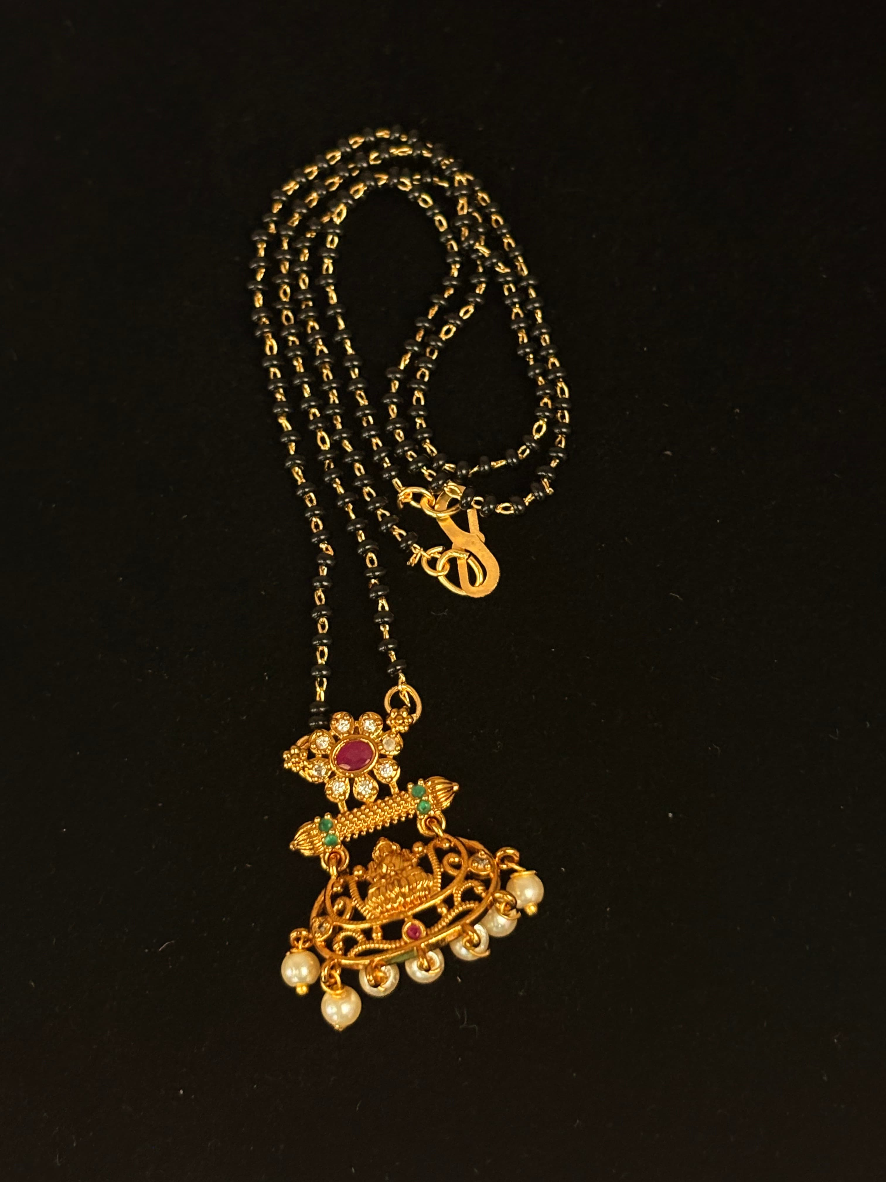 Mangalsutra with multiple black bead strands and gold-coloured floral pendant with pearl-like drops
