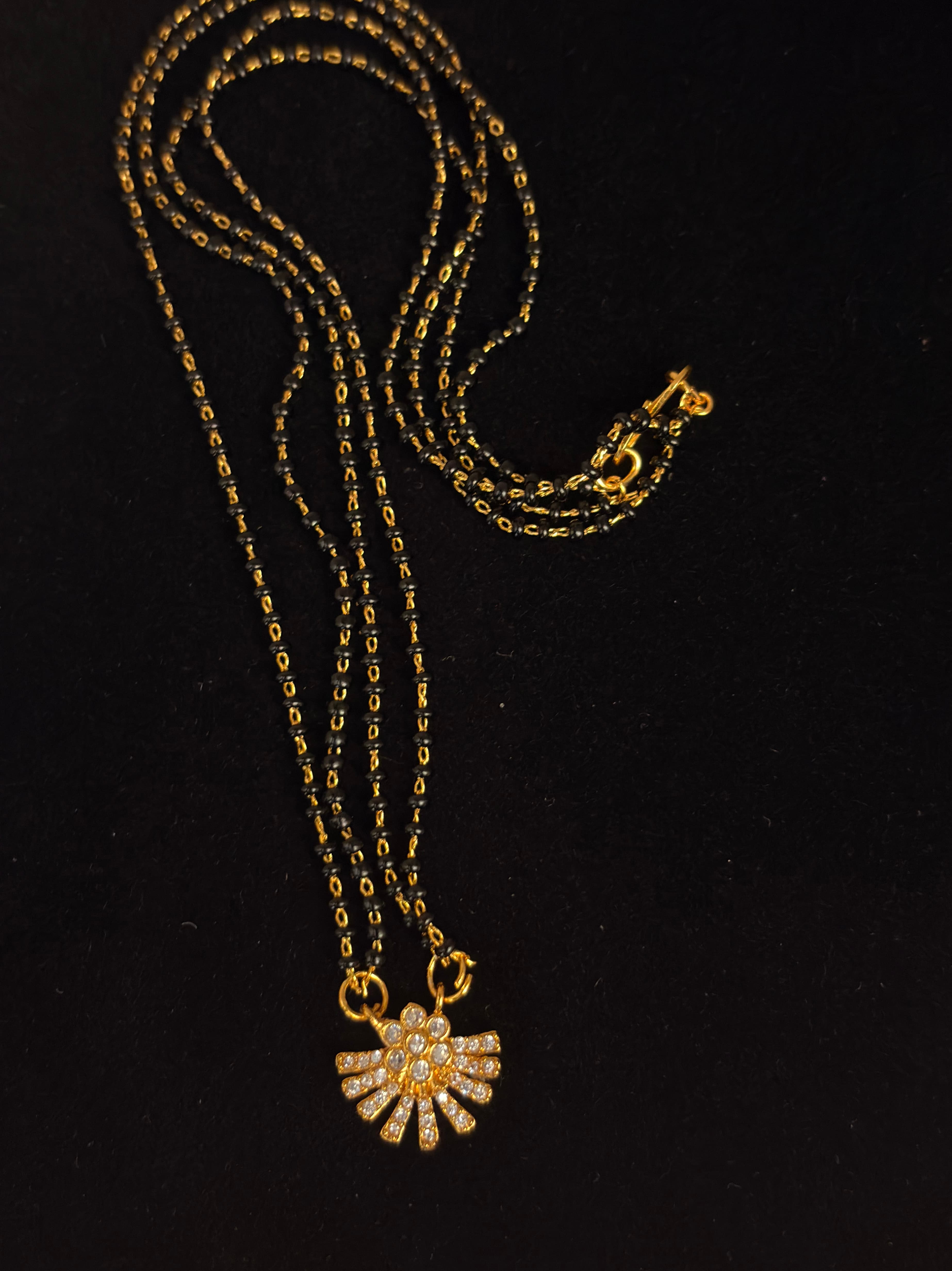 Multi-strand black bead mangalsutra with gold-tone links and a fan-shaped pendant with clear accents