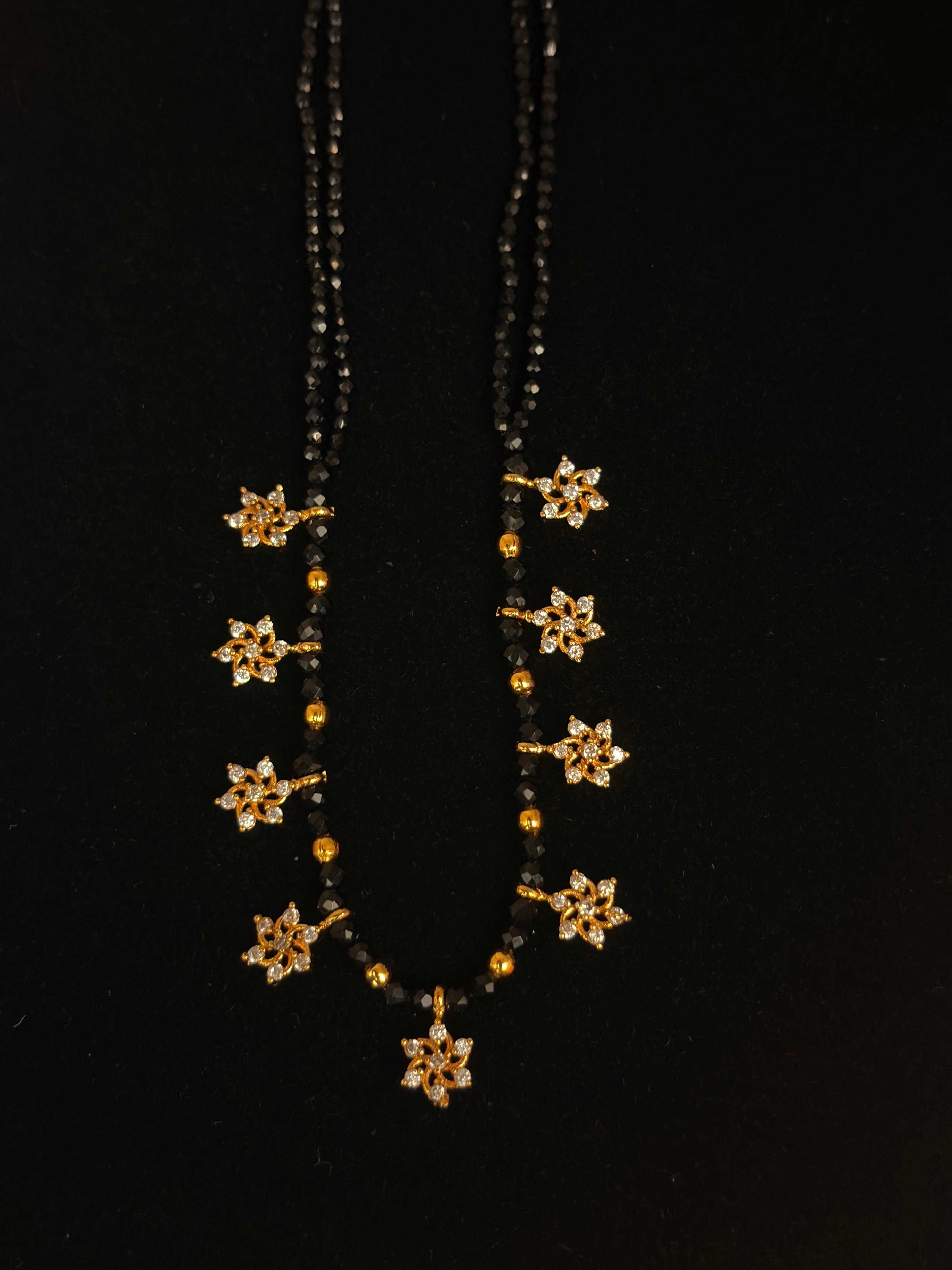 Double-strand black bead mangalsutra with gold-tone floral drop charms and clear sparkly accents