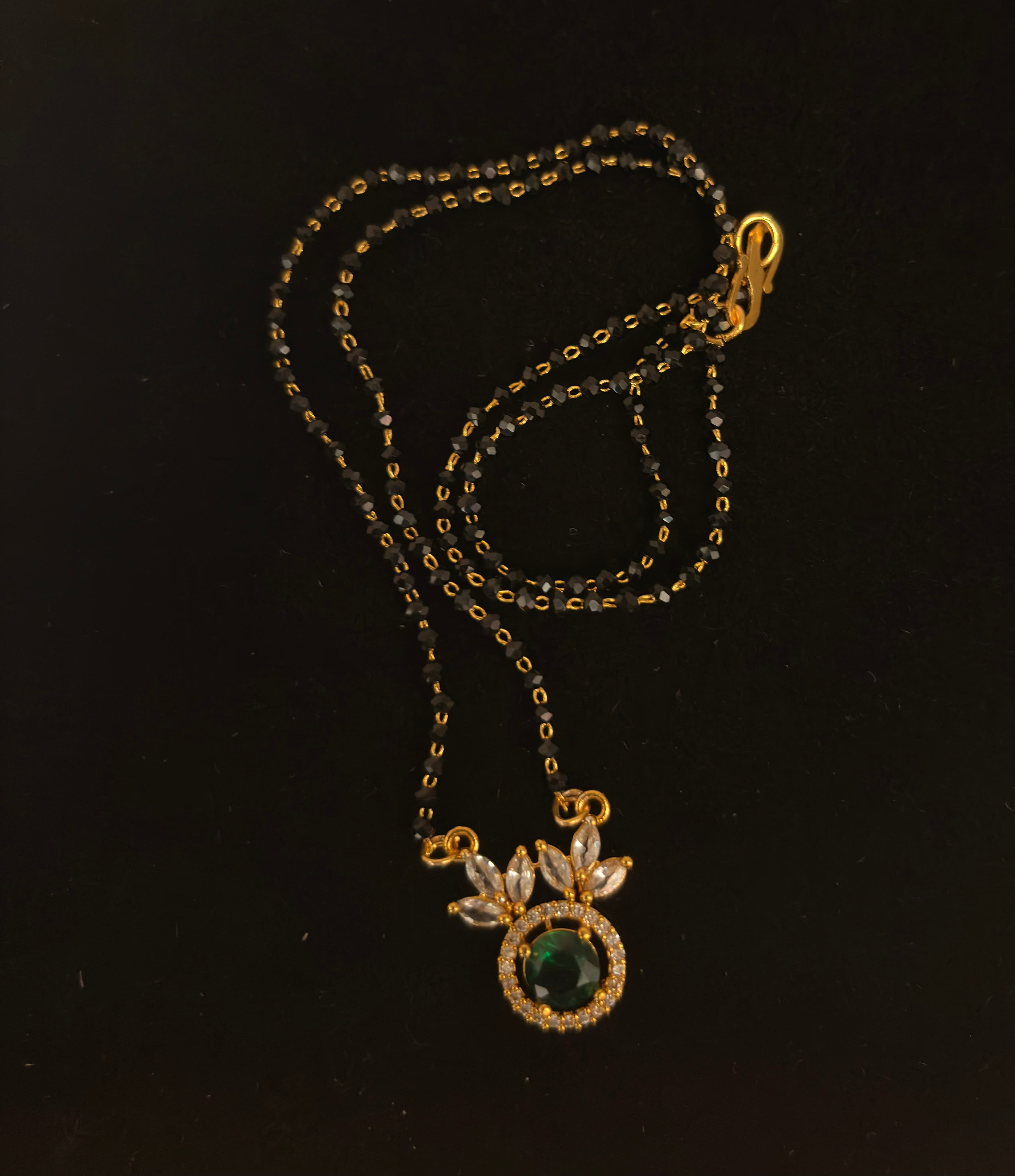 Mangalsutra with faceted black beads, gold-tone links and a green-centred floral pendant