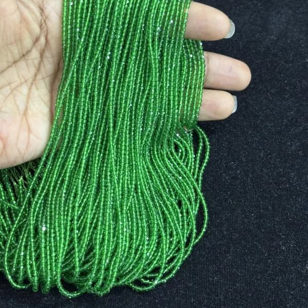 Multiple strands of small faceted green hydro beads held in a hand