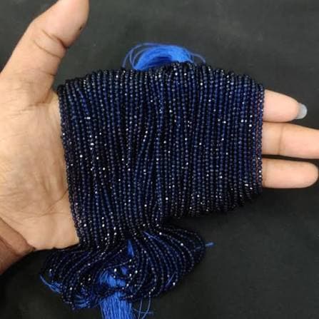 Strands of small dark navy blue faceted hydro beads held across a hand