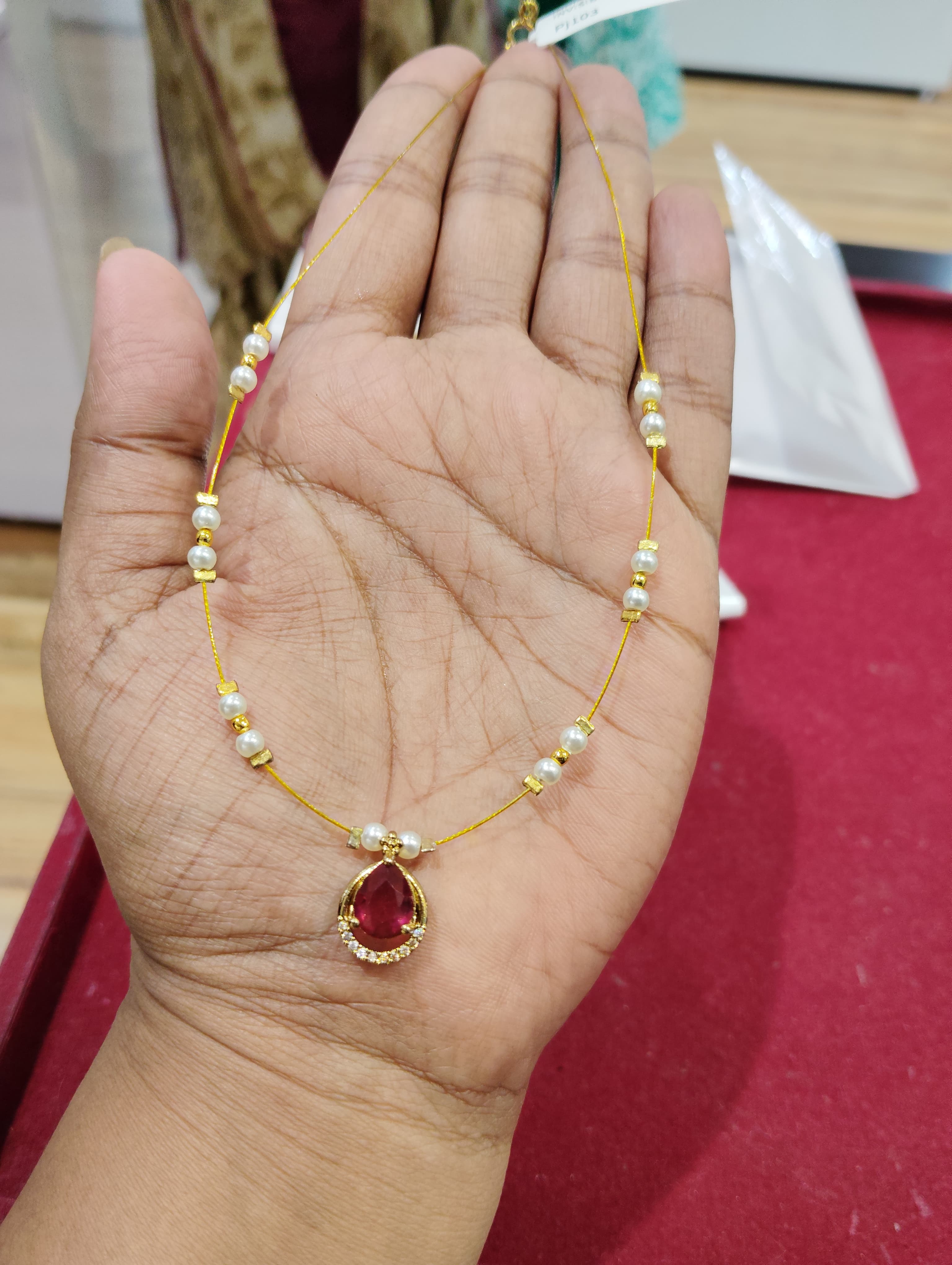 Thin gold-tone mangalsutra chain with white beads and red teardrop pendant with clear stones
