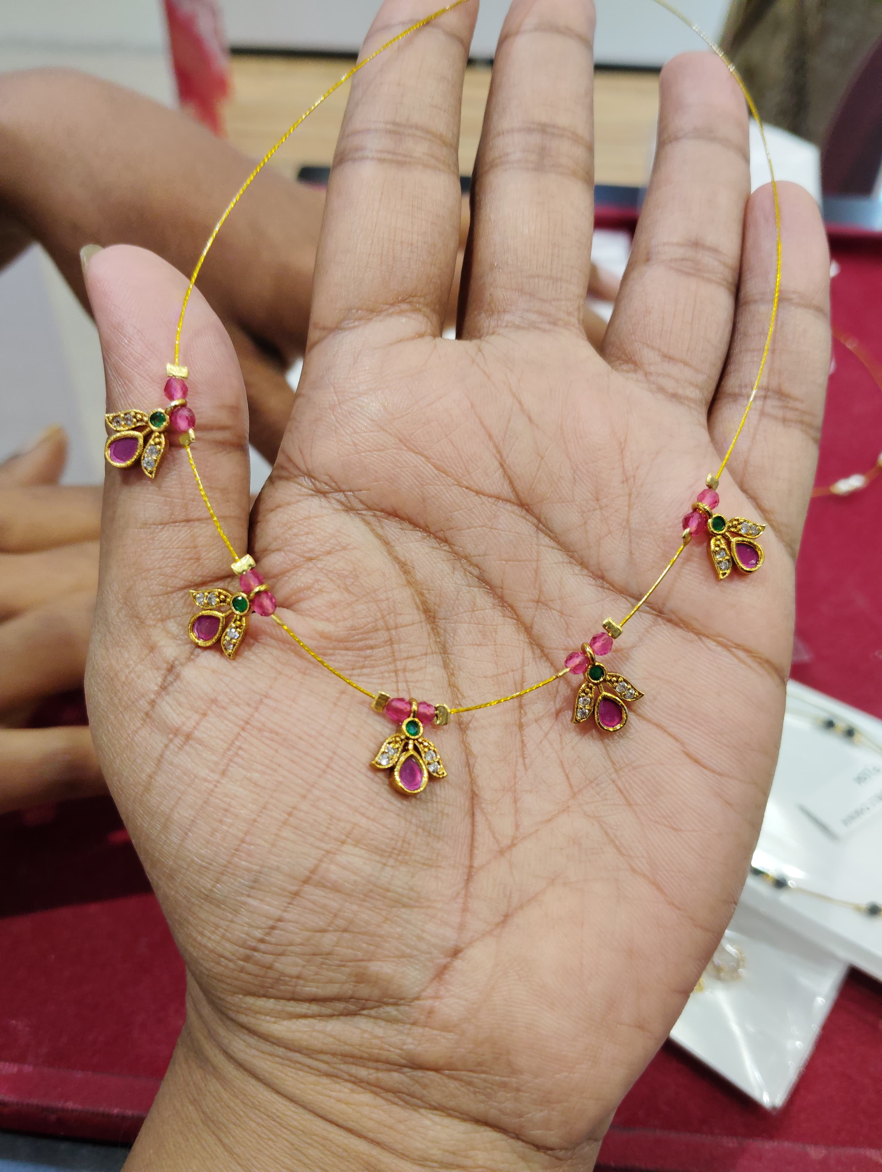 Slim gold-coloured mangalsutra with small pink teardrop and green round floral pendants on a fine thread