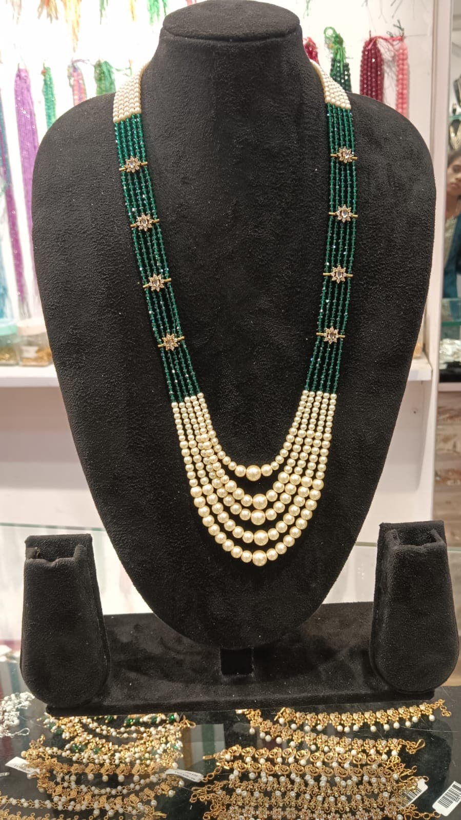 Layered necklace with five cream-coloured bead tiers and green bead strands with floral gold-tone spacers