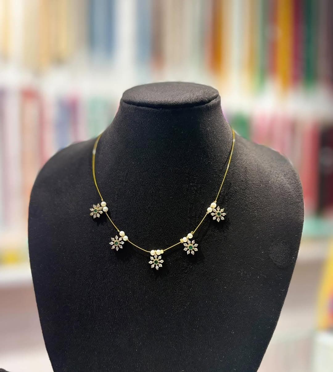 Slim gold-toned chain necklace with five small floral charms and pearly beads on a black display