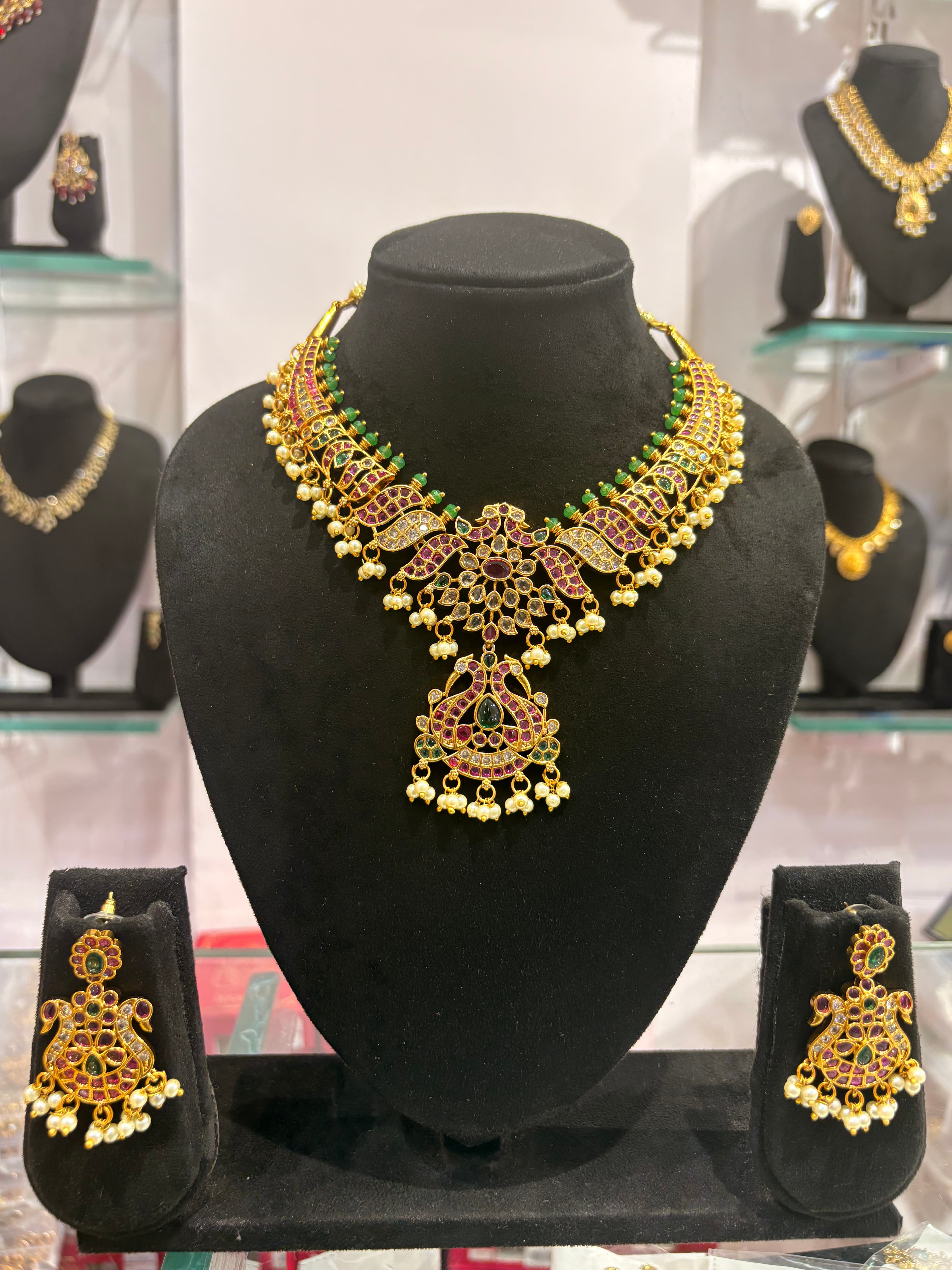 Gold-tone ornate necklace with pink and green accents and pearl-style danglers on black display