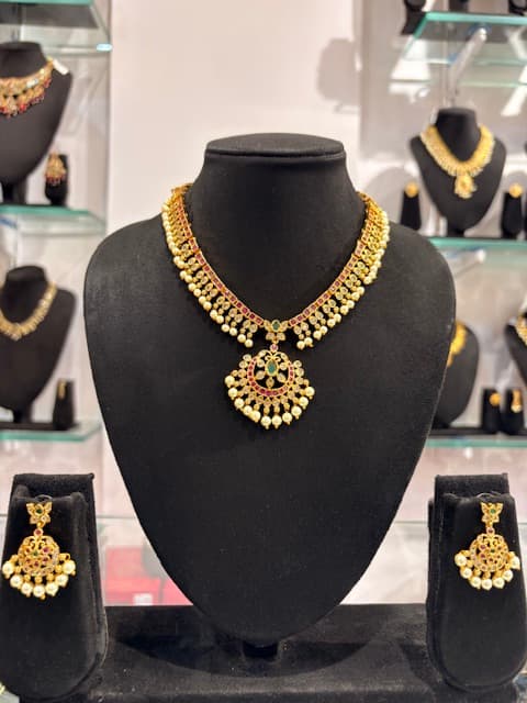 Gold-tone choker necklace with floral pendant, red and green accents and cream bead drops with matching earrings