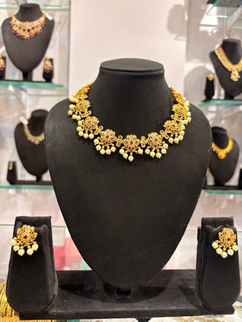 Gold-tone choker necklace with floral motifs, red accents and hanging pearl clusters with matching studs