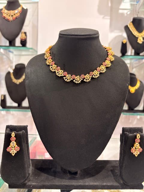 Gold-tone floral choker necklace with pink accents and matching drop earrings on black display