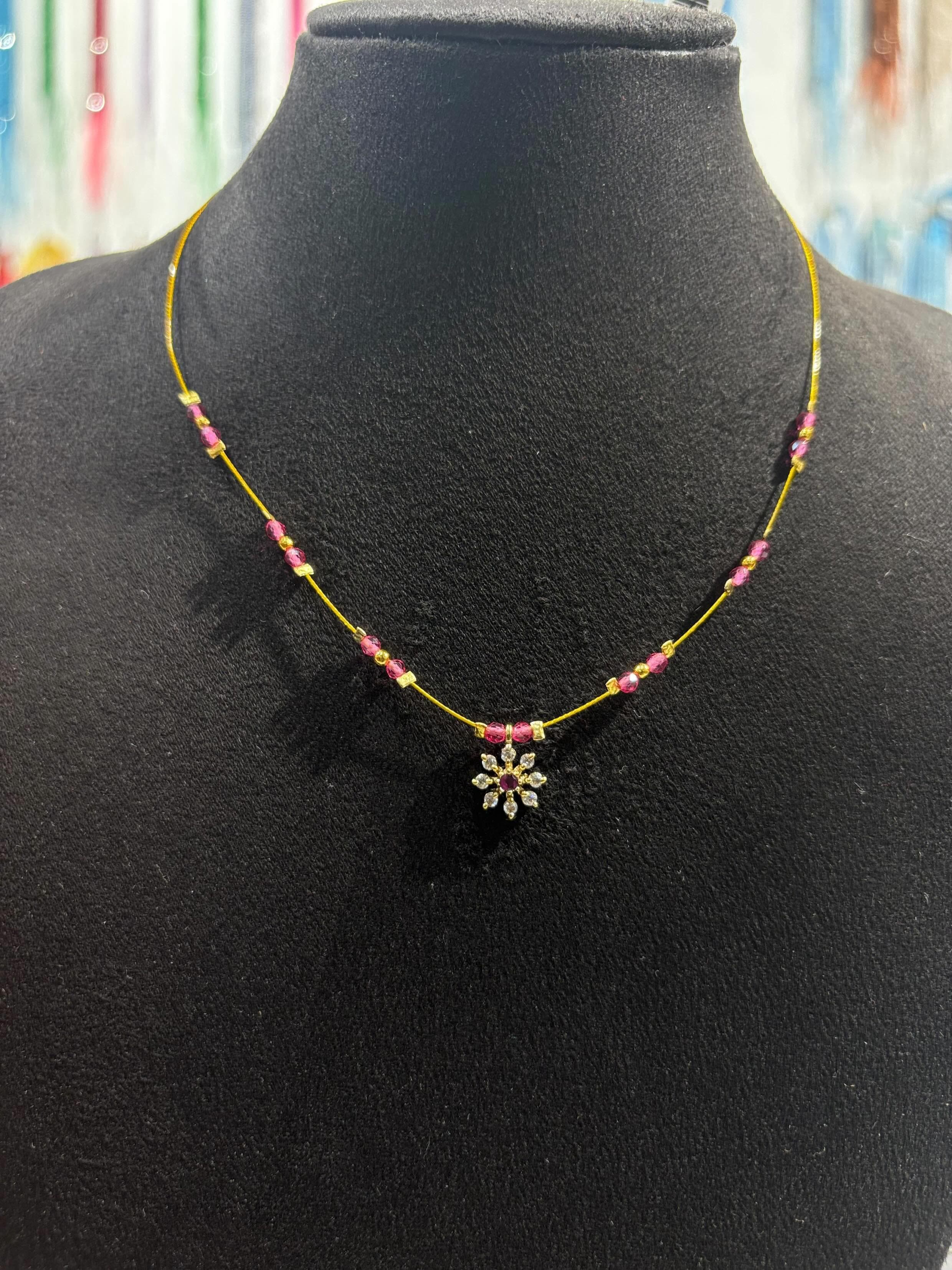 Thin yellow-thread necklace with pink beads and flower-shaped pendant on a black display